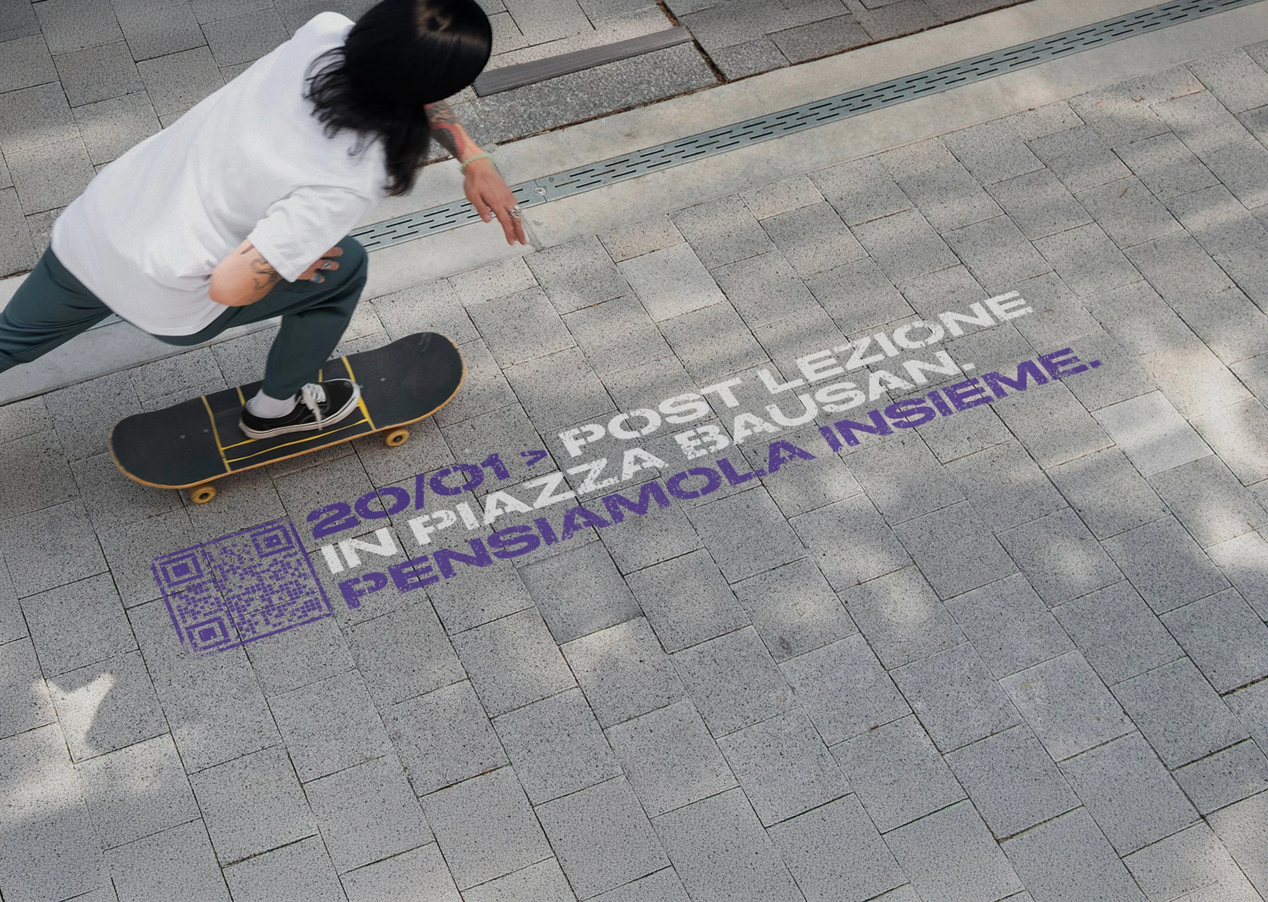 Floor graffiti Piazze Negate '20/01 POST LEZIONE IN PIAZZA BAUSAN. PENSIAMOLA INSIEME.' con QR code sulla pavimentazione, skater di passaggio
