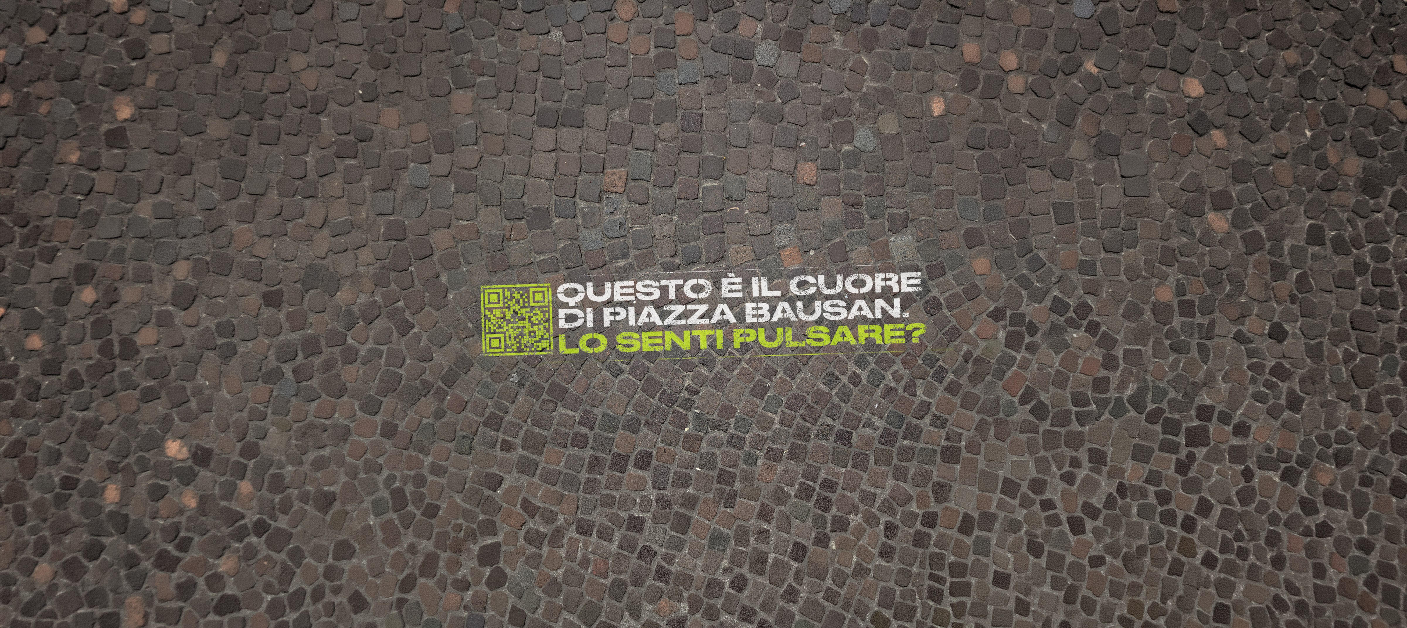 Floor graffiti in Piazza Bausan: 'Questo e' il cuore di Piazza Bausan. Lo senti pulsare?' con QR code, dipinto sul pavimento in porfido