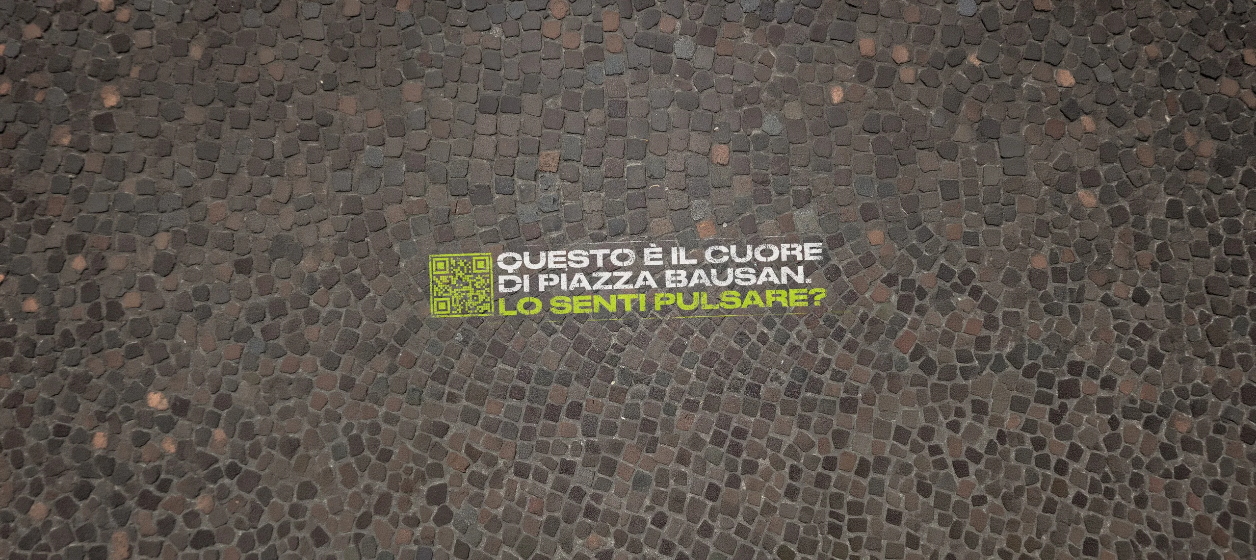 Floor graffiti in Piazza Bausan: 'Questo e' il cuore di Piazza Bausan. Lo senti pulsare?' con QR code, dipinto sul pavimento in porfido